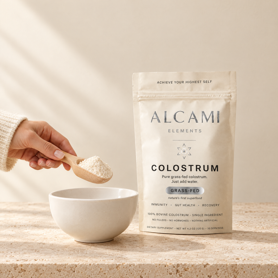 A scoop of Alcami Colostrum powder held over a bowl, with the pouch behind