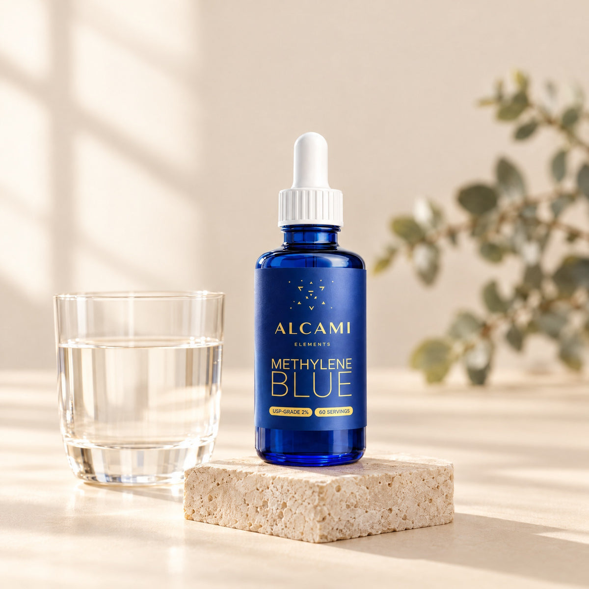 Alcami Methylene Blue dropper bottle on a stone tray beside a glass of water